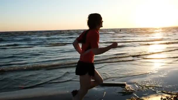 Man runs to the sea and is happy at the finish on the background of kitesurfers at sunset. — Stock Video