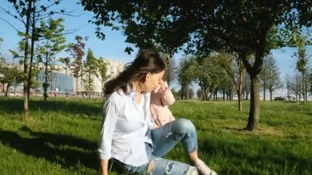 Jeune mère jouant avec son bébé dans le parc. Femme heureuse met sur le dos de l'enfant — Video