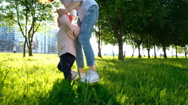 Anne parkta çim üzerinde günbatımında yürümek için küçük bir çocuk yardımcı olur. İlk adım, ağır çekim çocuk alır.