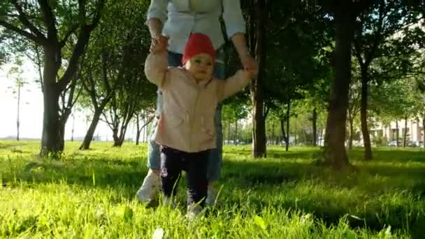 Щаслива дитина вчиться гуляти з матір'ю в парку на заході сонця . — стокове відео