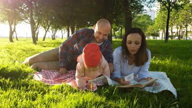 Mutlu aile çimenlerin üzerinde yatıyor ve günbatımı Park adlı bir çocukla bir piknik üzerine bir kitap okumak