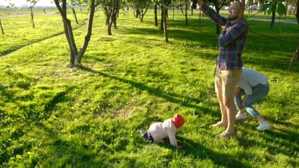 Joven padre tomando fotos de madre e hija jugando en el parque al atardecer. Familia feliz descansando y fotografiado en la naturaleza, cámara lenta — Vídeo de stock