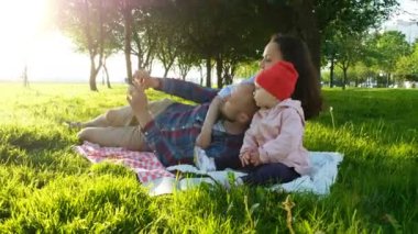Mutlu aile çarptırılmış döşeme ve selfie bir bebekle günbatımında parkta yapıyor. Babası kendilerini resimleri ile bebek alır.
