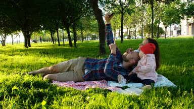 Mutlu aile üzerinde kareli döşeme ve selfie bir bebekle günbatımında parkta yapıyor. Anne bebeğim, kamera hareketi ile kendilerini resimleri alır