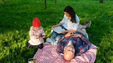 Genç aile doğa istirahat ediyor, küçük bir çocuk bir smartphone kollarına alır, annesi babası yalanlar üzerine bir ekose bir kitap okur