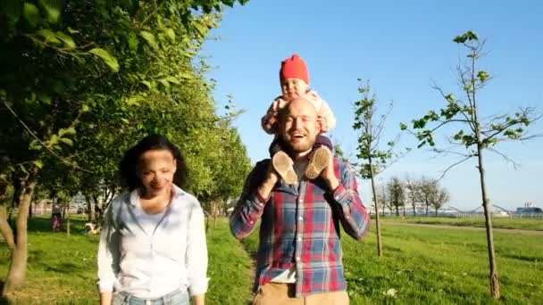 彼の父の肩の上に座って泣いている小さな女の子。若い家族が公園を散歩して夕日、お父さん怖い子、スローモーション. — ストック動画