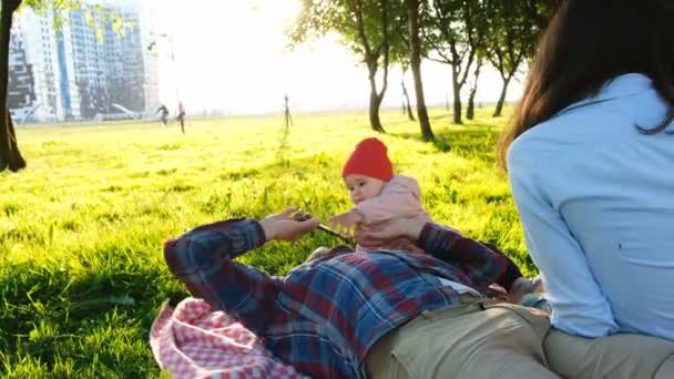 Familia joven está descansando en la naturaleza, un niño pequeño pide un teléfono inteligente, el padre le quita el teléfono al bebé — Vídeo de stock