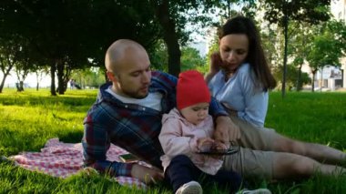Mutlu aile parkta çim üzerinde dinleniyor. Bir akıllı telefon elinde tutan genç çocuk.