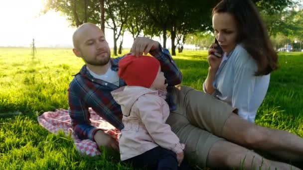 Little baby girl takes a smartphone and answers a phone call and talks close up. Happy family having a rest on a summer picnic in nature — Stock Video