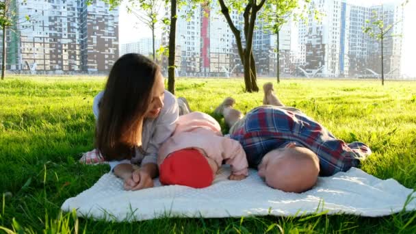 Ojciec i córka leżą z matki na trawie w parku w lecie. Szczęśliwa rodzina z małym dzieckiem odpoczynku w parku lato o zachodzie słońca — Wideo stockowe