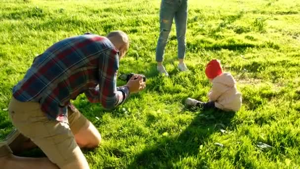 Jovem pai tirando fotos da filha no parque ao pôr do sol. Família feliz que tem um resto com a criança na natureza — Vídeo de Stock