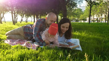 Mutlu aile çimenlerin üzerinde yatıyor ve bir piknik bir kitap okuyabilir ve çocukla günbatımında parkta oynamak..