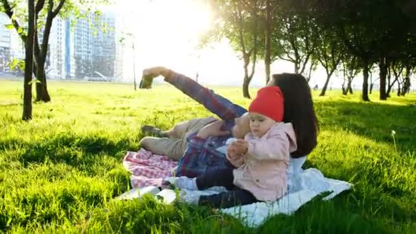 A família feliz está deitada no xadrez e fazendo selfie com um bebê ao pôr do sol no parque. Pai e mãe tiram fotos de si mesmos com o bebê — Vídeo de Stock