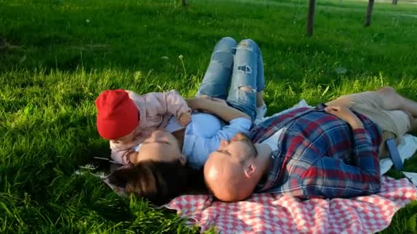 Happy family lies and rests on the nature, a small child takes a smartphone in his hands — Stock Video