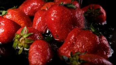 Siyah bir arka plan ağır çekim bir çilek üzerinde su döktü.