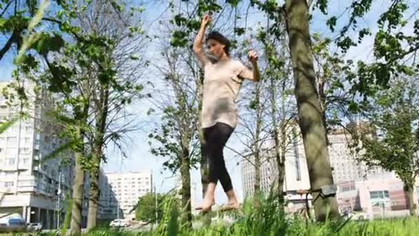 美しい少女は、都市公園におけるタイトなラインに沿って歩いています。Slackline 女性残高 — ストック動画