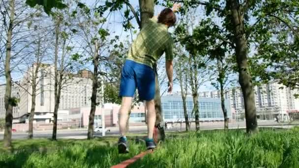 年轻的欧洲人在城市公园里走在一条狭窄的线上。那家伙在 slackline 的平衡. — 图库视频影像