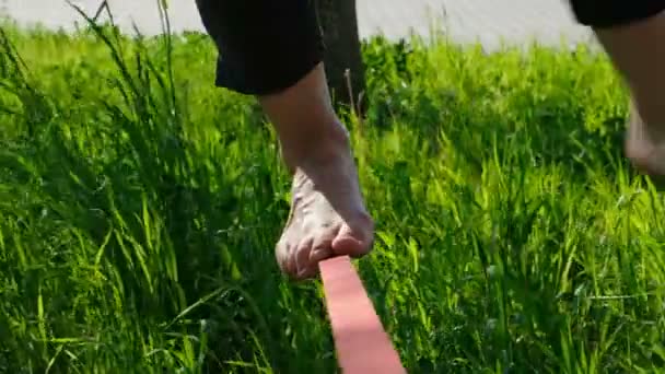Vrouw benen lopen langs een strakke lijn in een stadspark. Meisje van de voet balanceert op de slackline, gaat terug close-up — Stockvideo