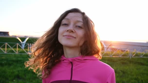 Retrato de uma bela mulher europeia ao pôr do sol em um fundo de estrada. Menina desportiva sorrindo e posando na câmera close-up, câmera lenta — Vídeo de Stock