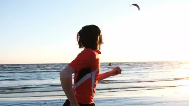 Homme courant le long de l'océan au coucher du soleil et lève les mains triomphalement et sautant à l'arrivée sur le fond de kitesurfers — Video