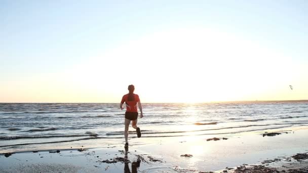 男は日没に合わせて実行し、日没時水にジャンプします。ランナーがフィニッシュ ライン、スローモーションでジャンプして手を上げる — ストック動画