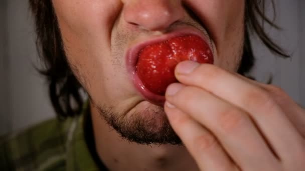 El hombre brutal está comiendo fresas jugosas de cerca. Chico hambriento repugnante mastica una gran baya madura con asco — Vídeo de stock