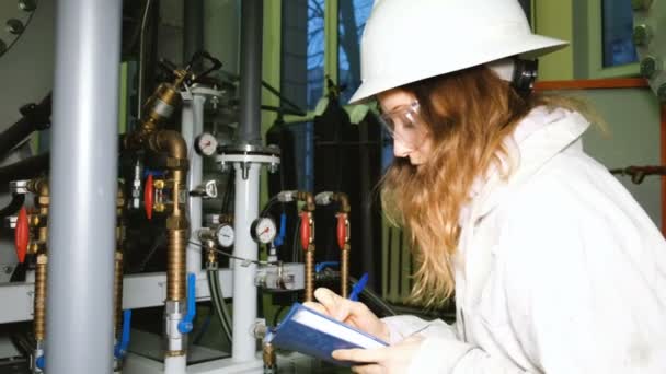 Flickan som ingenjör i en hjälm och goggles records data från tryckgivare i produktion rummet, mätare av Gasutrustning. — Stockvideo
