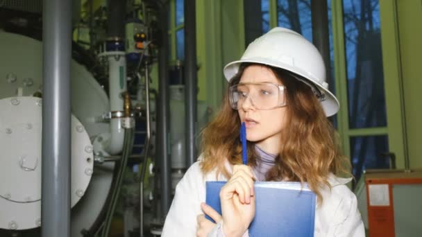 Niña ingeniero en un casco blanco examina cuidadosamente el equipo de gas y piensa . — Vídeos de Stock