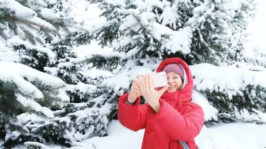 Karlı bir kış orman ağaçlarında bir arka plan üzerinde selfie aşağı ceket gülümseyen kız yapar