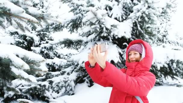 Mädchen in Daunenjacke macht Selfie vor verschneiten Bäumen im Winterwald — Stockvideo