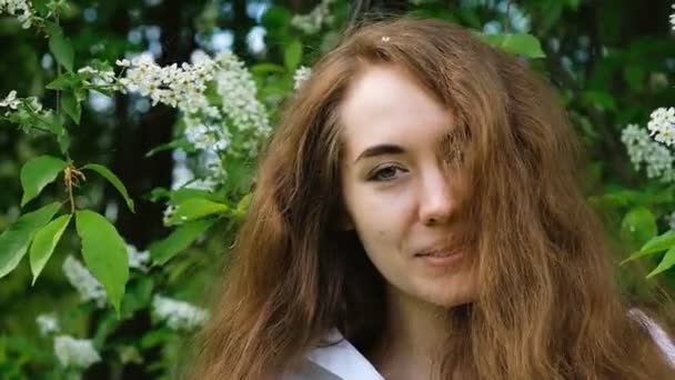 Porträt einer schönen jungen Frau, ein europäisches Mädchen lächelt und schickt einen Luftkuss in Blumen. Nahaufnahme, Zeitlupe. — Stockvideo
