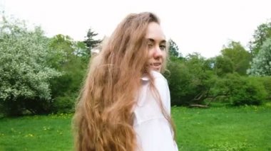 Kameraya poz çok uzun kıvırcık saçlı güzel bir genç kız portresi. Çekici bir kadın manken doğa yürüyüşleri, rüzgar saçlarını yavaş gelişir