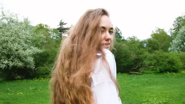 Porträt eines schönen jungen Mädchens mit sehr langen lockigen Haaren, das vor der Kamera posiert. eine attraktive Modefrau Modell geht in der Natur, der Wind entwickelt ihre Haare, Zeitlupe — Stockvideo