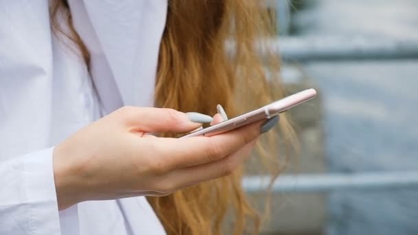 Biznes kobieta z długie paznokcie i włosy drukuje wiadomość bliska. Europejska dziewczyna używa smartfona w przyrodzie, w zwolnionym tempie — Wideo stockowe