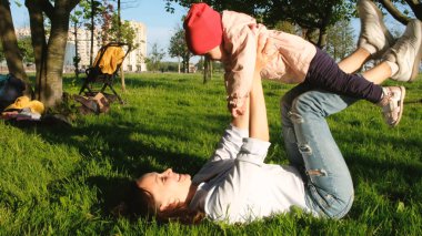 Anne ve bebek çim üzerinde yalan söylüyorsun, Anne ile bebeği parkta günbatımında oynuyor.