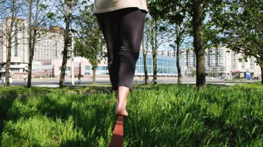 Avrupa kadın bir şehir parkı sıkı bir çizgi boyunca yürüyor. Arkasından slackline bakiyelere kız