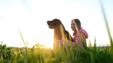 Köpek gün batımında sarılma ve gülüyor, evde beslenen hayvan çimenlerin üzerinde oturan ve doğada dinlenme ile genç kız kadın
