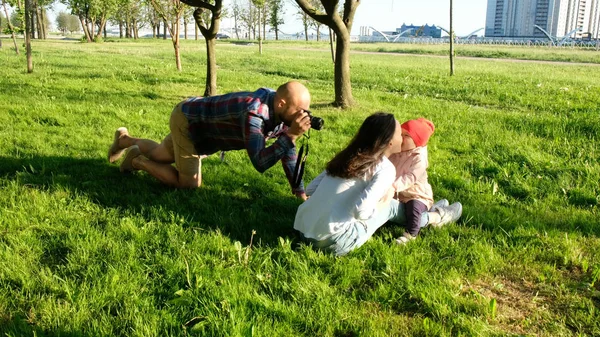Молодой отец фотографирует целующихся мать и дочь в парке на закате. Счастливая семья фотографирует на природе — стоковое фото