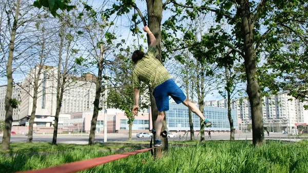 Młodych europejskich człowiek idzie przez linię mocno w parku miejskim. Facet jest równoważenie na slackline. — Zdjęcie stockowe