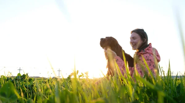 Vrouw met hond spelen bij zonsondergang, jong meisje met huisdier zittend op gras en ontspannen in de natuur — Stockfoto