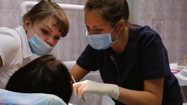 Врач-дантист объясняет молодому ассистенту лечение зубов, замедленную съемку. Клиент на ресепшене у дантиста — стоковое видео
