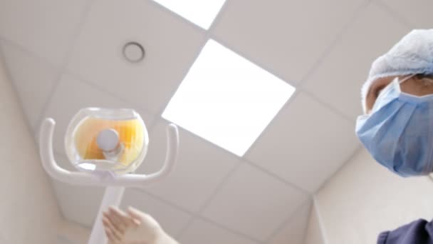 El dentista enciende la lámpara y se para sobre el paciente y trata los dientes. Sobre la recepción al médico del estomatólogo — Vídeo de stock