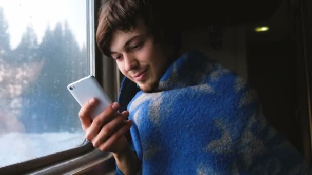 En man i en pläd på ett tåg och använder smartphone, 4k. — Stockvideo