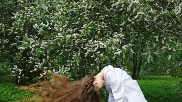 Una joven belleza de pelo largo con una camisa blanca arroja su pelo rizado hacia arriba en el medio del bosque contra en el parque — Vídeo de stock