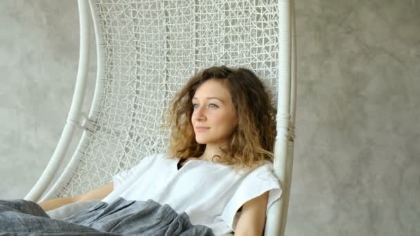 Young European girl in a linen dress keep calm and swinging in a hammock chair, enjoying the rest. Beautiful girl dreams and swings in the loft interior of the house — Stock Video