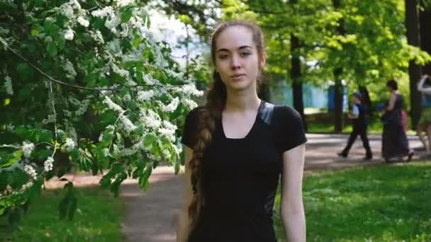 Hermosa joven con una larga trenza camina en el parque, ir directamente a la cámara, cámara lenta. Atractiva mujer europea posando y mirando recto — Vídeos de Stock