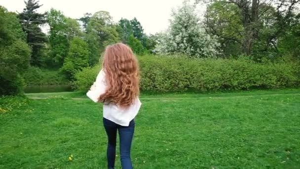 Европейская девушка с длинными вьющимися волосами бегает в парке. Очень длинные волосы развеваются на ветру, медленное движение — стоковое видео