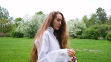 Çok uzun kıvırcık saçları Avrupa kız kabarcıklar sağlar ve doğa üzerinde çalışır. Genç kadın modeli parkta eğleniyor, saç rüzgar, ağır çekim çırpınan