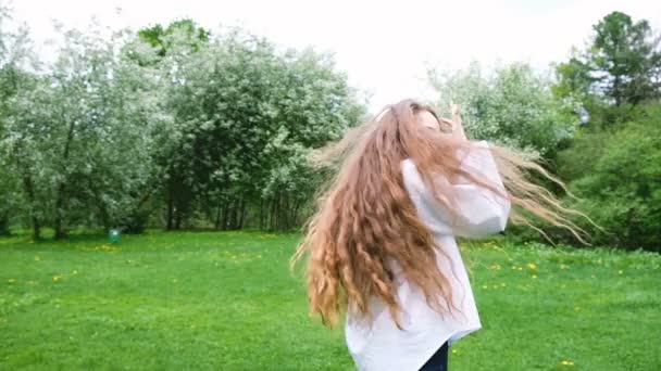 Europäisches Mädchen mit sehr langen lockigen Haaren lässt Blasen sprudeln und rennt auf die Natur los. sexy weibliches Model hat Spaß im Park und winkt, Haare flattern im Wind, Zeitlupe — Stockvideo