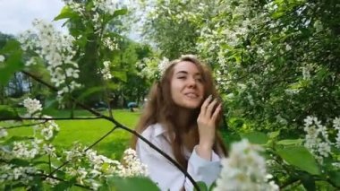 Çiçek açması kuş kiraz kamerada poz çok Avrupa kız modeli. Park, ağır çekim uzun kabarık saçlı ve bir şube başında bir kadın fotoğrafı